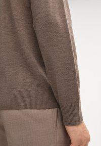 Brauner Strickpullover mit geripptem Saum und Bündchen, gefertigt aus weichem Material mit glatter Textur. Die Seitenansicht zeigt ein figurnahes Design.