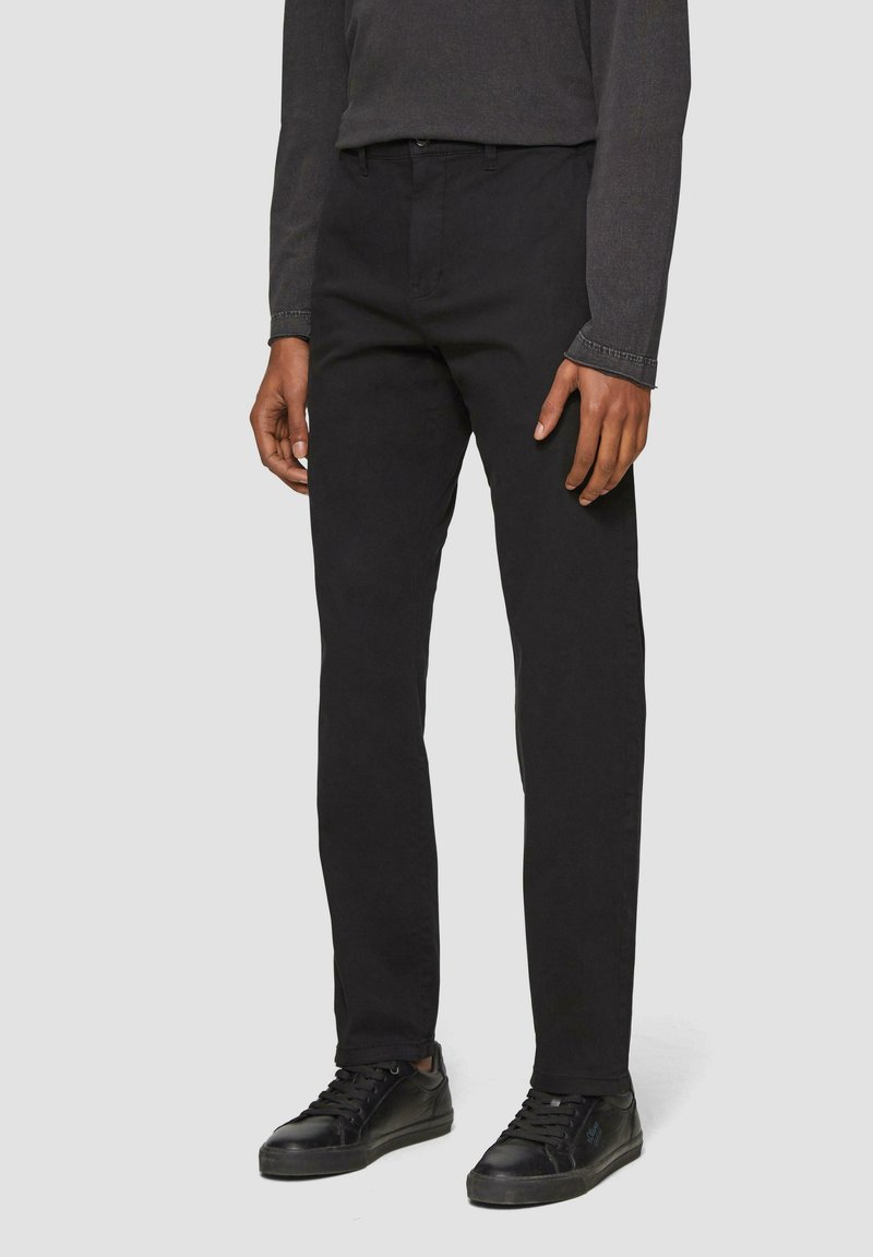 Zwarte katoenen broek met een rechte snit, voorzien van een standaard tailleband en subtiele stiksels. Gekleed met zwarte sneakers.