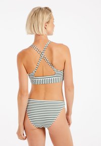 Dryžuotas bikini komplektas, kuriame dominuoja žalia ir balta spalvų gama. Viršutinė dalis turi kryžminį nugaros dizainą su platesnėmis juostelėmis ir išpjovomis.