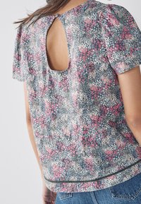 Top w kwiatowy wzór z lekkiego materiału, z krótkimi balonowymi rękawami, z tyłu z wycięciem w kształcie łezki oraz dołem ozdobionym dekoracyjną lamówką.