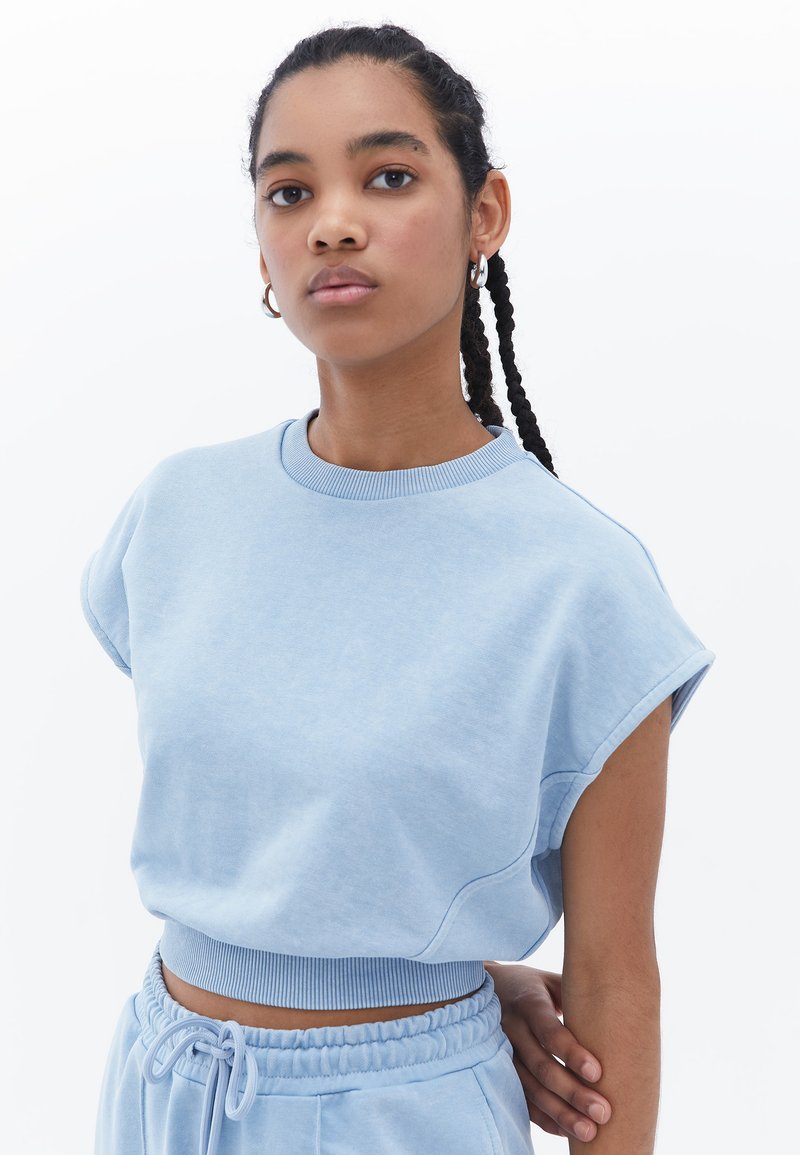 Sudadera corta de color azul claro con mangas anchas y cuello de canalé. Textura suave, combinada con pantalones de chándal a juego que cuentan con una cinturilla elástica.