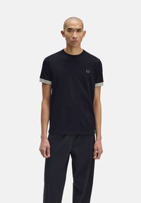 T-shirt nero a maniche corte con polsini striati in verde e bianco. Presenta un piccolo emblem sulla parte del petto. Il tessuto ha una consistenza liscia.