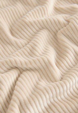 Beżowy, prążkowany pled z miękkiej, teksturowanej tkaniny, prezentujący naprzemienne wzniesione i płaskie paski w przytulnym, pikowanym wzorze.