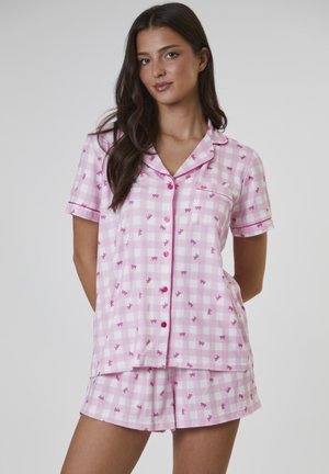 Roze geruit pyjama-ensemble met een shirt met korte mouwen en een zakje, en bijpassende korte broek, afgewerkt met kleine roze strikpatronen en knopen.