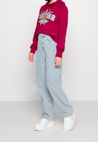 Person wearing a magenta hoodie with a cartoon deer and light blue high-waisted wide-leg jeans and white platform sneakers.