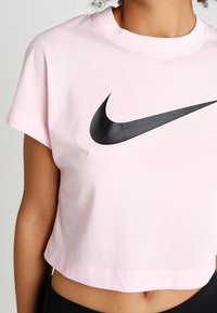 Rosa kortärmad t-shirt i bomull, med en stor svart Nike swoosh-logotyp på framsidan. Kort ärm och rund halsringning.