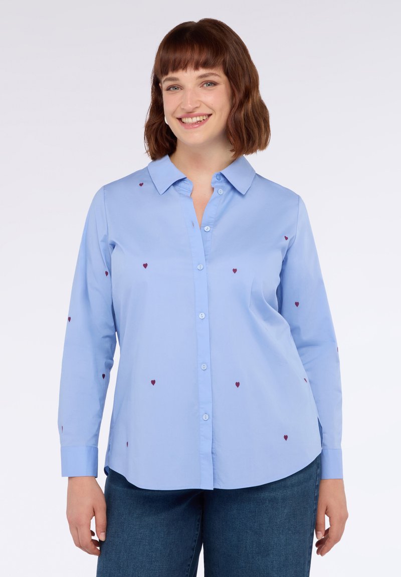 Camicia azzurro chiaro con bottoni, caratterizzata da piccoli cuori rossi ricamati, maniche lunghe e colletto, realizzata in un tessuto morbido.