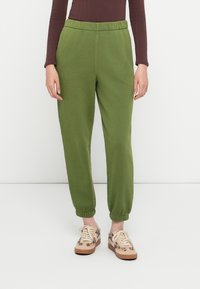 Pantalones de chándal verdes con cintura elástica, puños ajustados y una textura suave, combinados con zapatillas de deporte con estampado.
