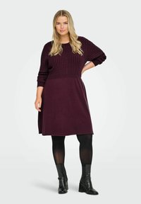 Bordo adīts kleita ar ribotu augšdaļu, garām piedurknēm un platām svārka malām. Saskaņota ar melniem potīšu zābakiem un necaurspīdīgām zeķbiksēm. Gluda tekstūra.