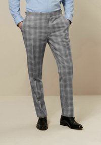 Pantalons à carreaux gris avec une coupe ajustée, dotés d'une taille plate et de poches latérales. Portés avec des chaussures noires et une chemise bleu clair.