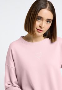 Roze sweatshirt met een relaxed fit, voorzien van een witte geborduurde hartdetail op de borst. Zachte textuur en ronde halslijn.