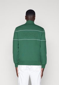 Felpa verde con collo alto, logo ricamato "BOSS", due strisce bianche orizzontali sulla schiena, polsini e orlo a costine.