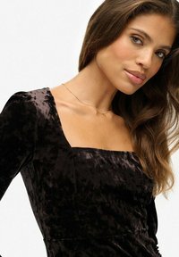 Schwarzes Samtkleid mit quadratischem Ausschnitt und langen Ärmeln, das eine weiche Textur und leichten Glanz aufweist. Subtile Details verleihen Tiefe.