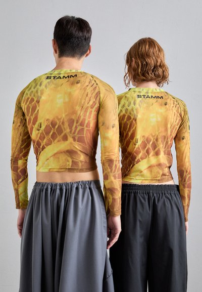 Langermede crop tops i nyanser av gul og oransje med et nettlignende mønster. Begge har på seg grå, elastiske bukser med midje. Merking bak.