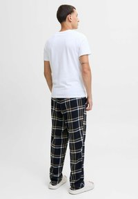 Maglietta bianca in cotone a maniche corte abbinata a pantaloni in flanella a quadri blu navy con linee beige e bianche, indossati con scarpe chiare.