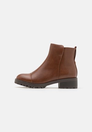Bottines en simili cuir marron avec un bout arrondi, des panneaux élastiques sur les côtés et un talon bloc. Surface texturée et détails de semelle extérieure robuste.