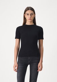 Svart kortermet t-skjorte laget av mykt stoff, med rund hals og en tettsittende design, sammen med mørke jeans.