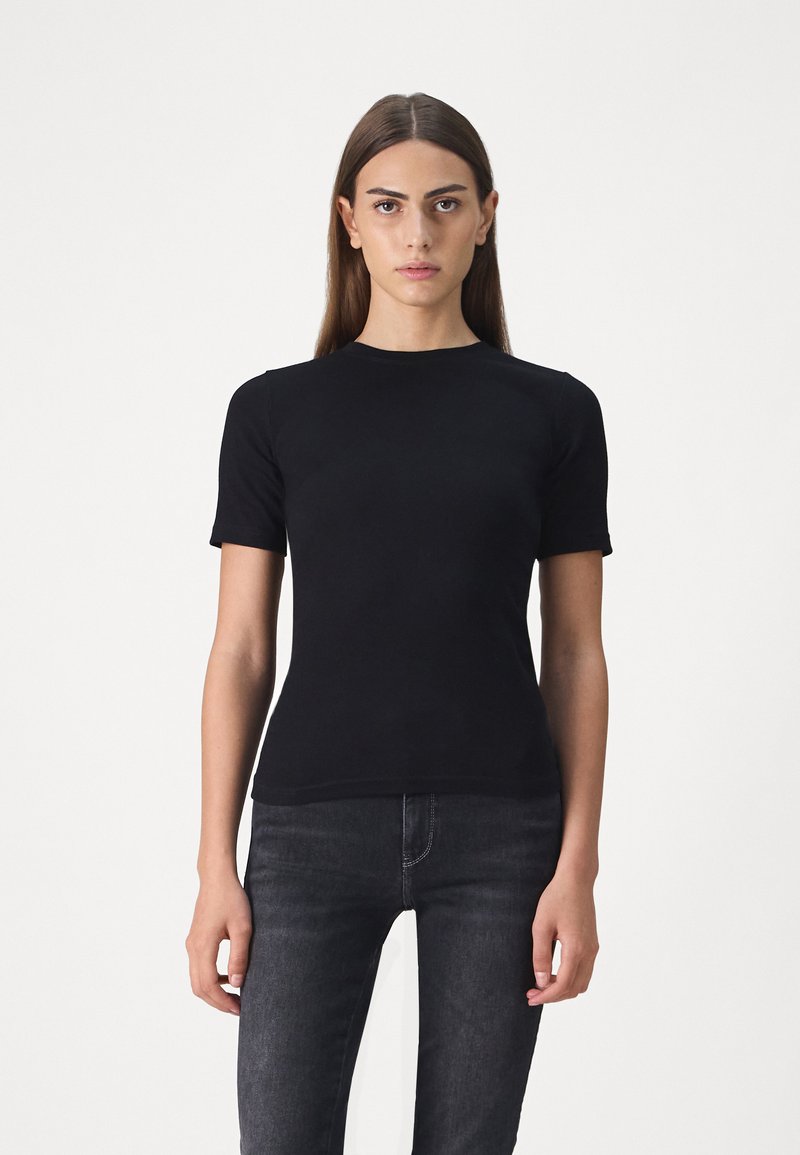 Svart kortermet t-skjorte laget av mykt stoff, med rund hals og en tettsittende design, sammen med mørke jeans.