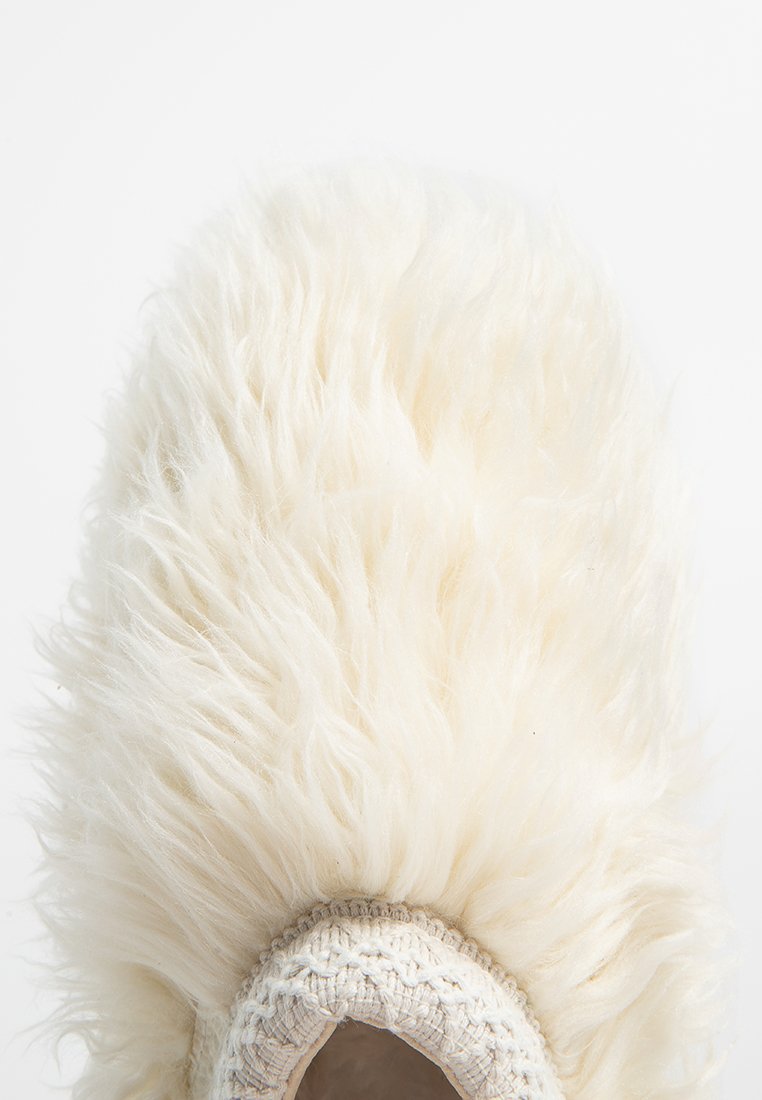 Ciabatta di pelliccia bianca foderata con un tessuto intrecciato texturizzato attorno all'apertura, caratterizzata da un aspetto morbido e soffice e una forma arrotondata.