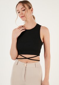 Mustmustelane ribagaheline crop-top, millel on ümmargune kaelus ja ristikujuline kaunistus seljal. Kombineeritud beežide kõrge vöökohaga pükstega, millel on nööbiga detail.