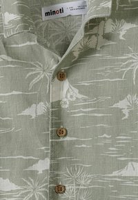 Camicia in lino verde con motivo palme, con abbottonatura frontale e bottoni in legno, colletto aperto. Tessuto leggero con dettagli strutturati.