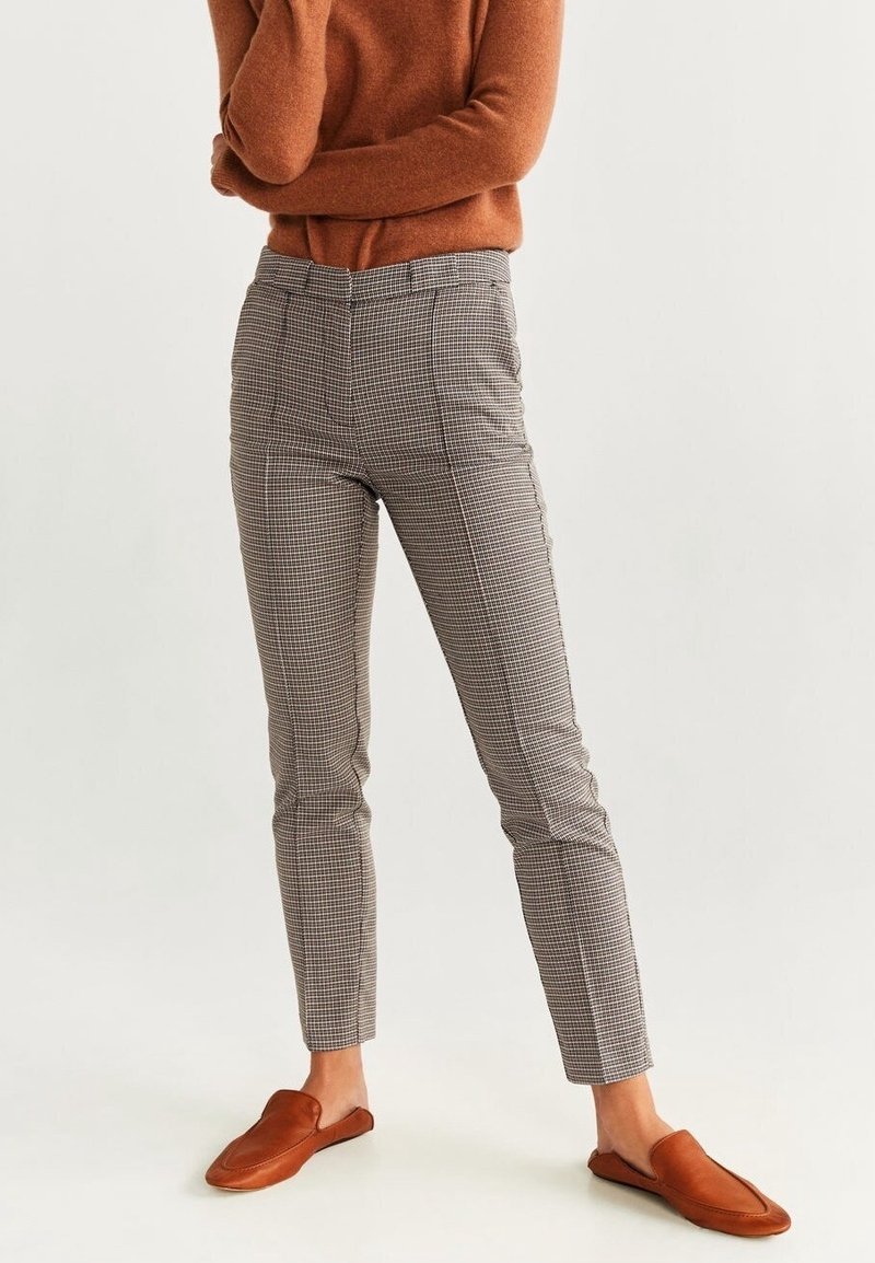 Pantalon ajusté à carreaux, avec une coupe slim, présentant un motif beige et brun. Associé à des chaussures brunes à enfiler et un pull couleur rouille.