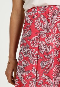 Jupe rose avec un motif de feuilles botaniques blanches. Fabriquée en matériau léger, elle a une texture lisse et une taille élastique.