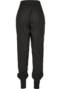 Pantalon de jogging noir en tissu lisse, doté d'une taille élastique et de poignets aux chevilles pour un ajustement fuselé. Pas de poches visibles.