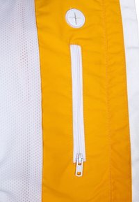 Żółto-biała tkanina z kieszenią na zamek błyskawiczny, o gładkiej fakturze i ozdobie w postaci guzika. Projekt zawiera elementy siateczkowe.