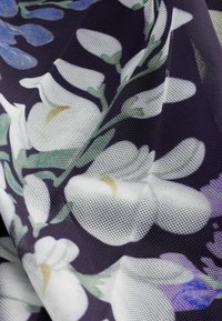 Tissu en mesh floral dans des tons de blanc et de bleu sur un fond violet foncé, présentant une texture douce et des motifs floraux complexes.