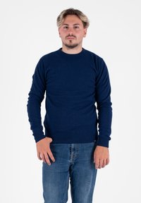 Ciemnoniebieski sweter z okrągłym dekoltem, wykonany z miękkiego materiału, z długimi rękawami i prążkowanymi mankietami, w połączeniu z jasnoniebieskimi dżinsami.