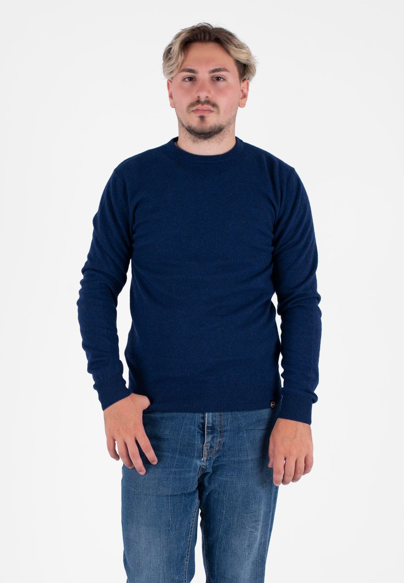 Ciemnoniebieski sweter z okrągłym dekoltem, wykonany z miękkiego materiału, z długimi rękawami i prążkowanymi mankietami, w połączeniu z jasnoniebieskimi dżinsami.