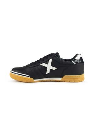 Zapatilla deportiva negra de caña baja con una X blanca en el lado, suela de goma color caramelo, cordones negros y cuello acolchado mostrada en perfil lateral sobre fondo blanco.