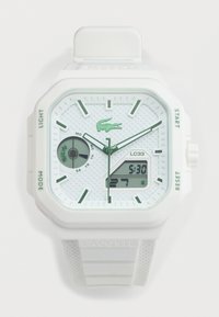 Λευκό ρολόι χειρός Lacoste με αναλογική και ψηφιακή οθόνη, πράσινους δείκτες ωρών, ένδειξη ημέρας και υφασμένο λουράκι με λογότυπο.