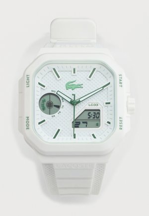 Biely hodinky Lacoste s analógovým a digitálnym displejom, zelenými hodinovými značkami, ukazovateľom dňa a štruktúrovaným remienkom s logom.