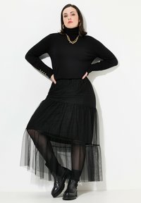Schwarzer Rollkragenpullover mit geripptem Textur, kombiniert mit einem geschichteten schwarzen Tüllrock. Getragen mit klobigen schwarzen Stiefeletten und einer goldenen Kettenhalskette.