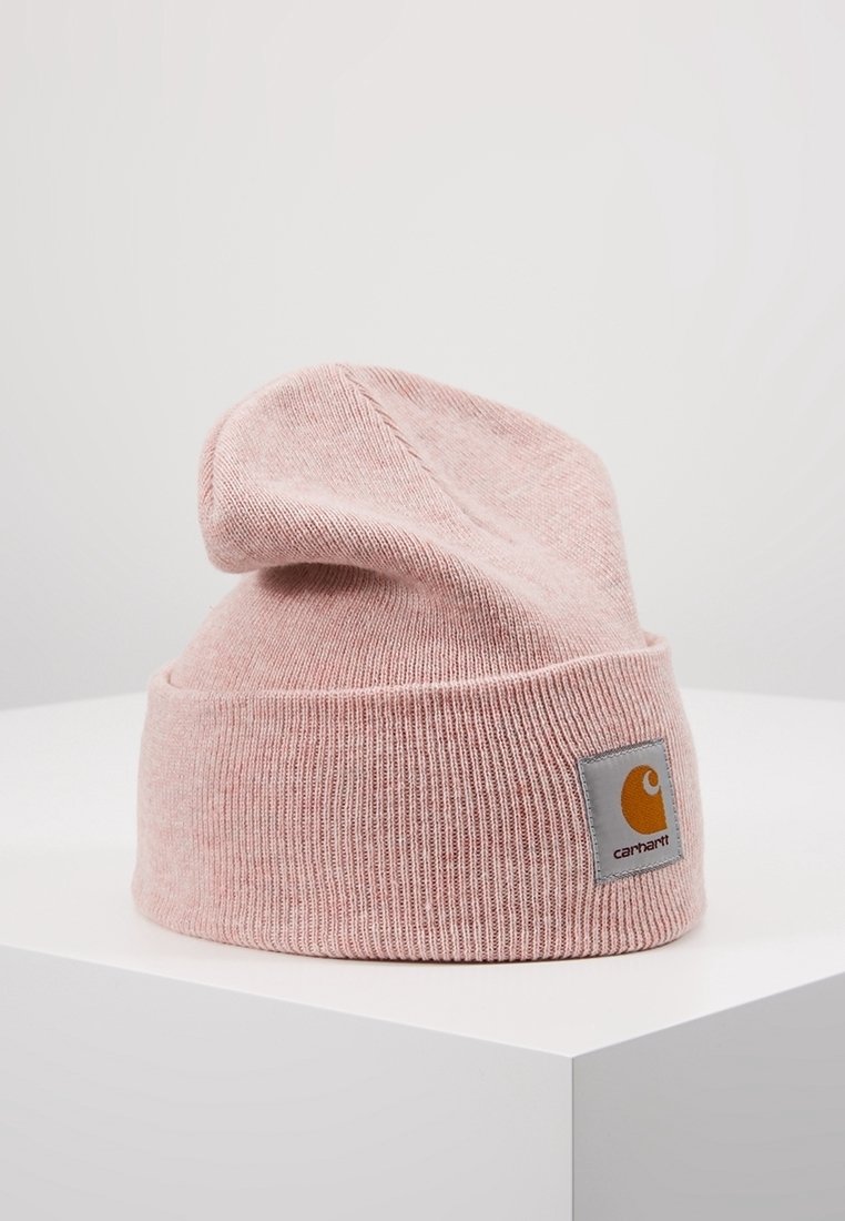 Bonnet tricoté rose doux avec un revers plié et un patch logo Carhartt carré sur le devant, posé sur une surface blanche.