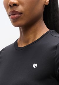 Μαύρο T-shirt με κοντά μανίκια από απαλό ύφασμα που διαθέτει λευκό λογότυπο στην αριστερή πλευρά του στήθους και στρογγυλή λαιμόκοψη.