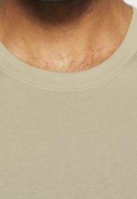 Camiseta de algodón verde olivo con cuello redondo acanalado, que presenta una textura suave y un ligero brillo en la tela.