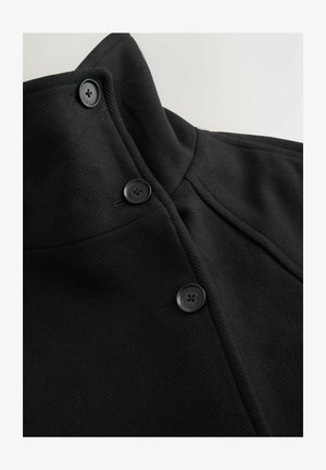 Melna jaka ar augstu apkakli, diviem melniem pogām un teksturētu audumu ar redzamām šuvēm.