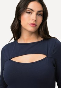 Marineblaues Langarmoberteil mit einem Ausschnittdesign. Hergestellt aus glattem Stoff mit einem weiten Ausschnitt und einer figurbetonten Silhouette.