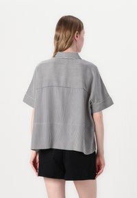 Camisa de manga corta a rayas con cuello, que presenta rayas alternas en blanco y negro, un corte holgado y un diseño de espalda partida.