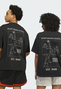 Zwart katoenen t-shirt met witte lijntekeningen van basketbalspelers op de achterkant, met de tekst "SPORT DESIGN STUDIO" en "EST. 1949" eronder.