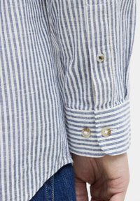 Camisa a rayas con líneas azules y blancas, con puños abotonados y un dobladillo curvado. Fabricada con un tejido ligero y de apariencia texturizada.