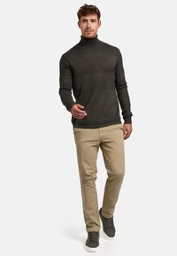 Mørk grønn genser med høy hals og teksturerte horisontale striper, kombinert med lys beige chinos og grå sneakers. Enkel, moderne design.