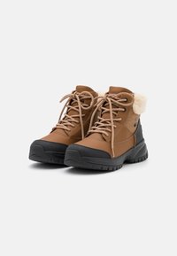 Botas de tobillo impermeables marrones con ribete de piel sintética beige, puntera redonda, suelas de goma negras, y diseño de cordones con acentos de tela texturizada.