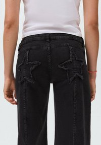 Črne denim hlače z raztrganimi zvezdastimi obliži na zadnjih žepih, z ravnim krojem in srednje visokim pasom.