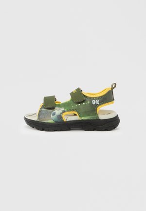 Sandales pour enfants avec dessus synthétique vert, accents jaunes, brides Velcro ajustables et semelle extérieure en caoutchouc noir texturé.