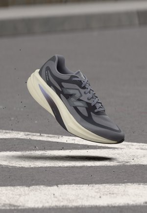 Сив и черен маратонка New Balance с дебела бяла подметка, плаващ над асфалт с бели пътни маркировки.