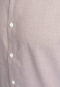 Chemise rose clair à boutons, en tissu texturé, dotée de boutons blancs et d'un motif tissé subtil. Gros plan sur la zone du col.